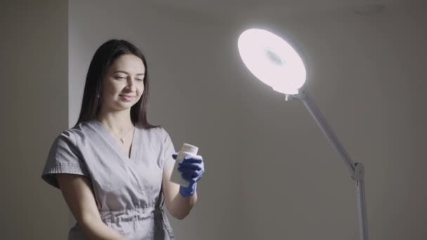 Sourire femelle épilation maître secoue emballage de talc, versé près de la lampe — Video