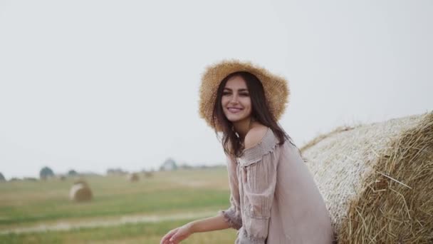 Hermosa chica en el sombrero posa en haycock para la cámara y riendo — Vídeos de Stock