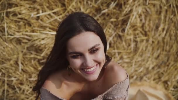 Impresionante morena con el pelo que sopla sonriendo en el pajar entre el campo en la cámara — Vídeos de Stock