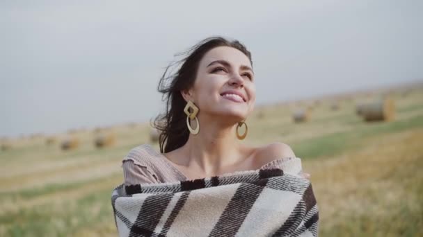 Chica bonita envolver en cuadros teniendo alegría durante el fuerte viento en el campo de heno espacioso — Vídeos de Stock