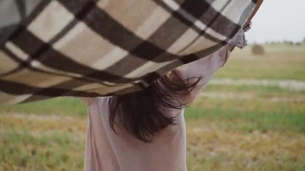 Ragazza cammina sul campo con il plaid, lo lascia cadere durante il vento e si gira con il sorriso — Video Stock