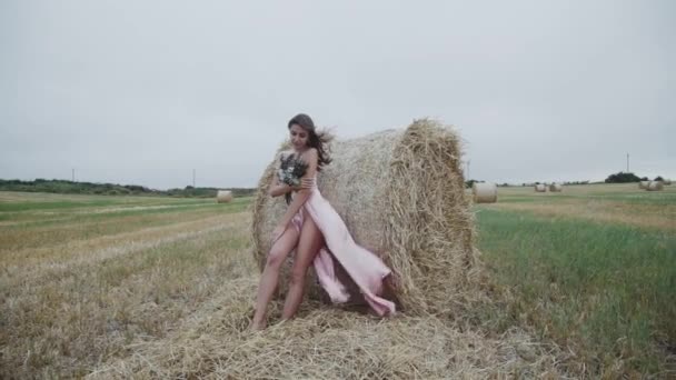 Senhora deslumbrante em soprando vestido de noite com buquê fica em poses no palheiro — Vídeo de Stock