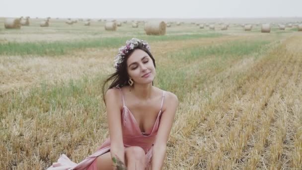 Elegantní dáma v šatech s květinami sedí na strništi v poli a pózuje — Stock video