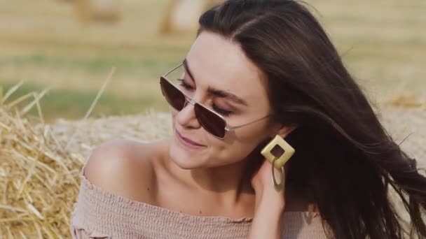 Porträtt av lycklig kvinna i solglasögon med blåsande hår ler mot höstack — Stockvideo