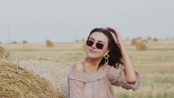 Gyönyörű nő napszemüvegben simogatások fúj haj és meztelen váll a területen — Stock videók
