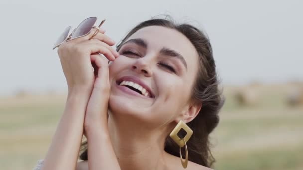 Portrait of happy woman smiling light at windy nature with sunglasses in hands — Stock Video