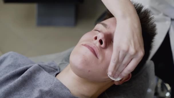 Szoros kilátás kozmetikusok kezét törölje a man arcát pamut tamponnal stúdióban — Stock videók