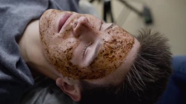 Güzellik uzmanlarının elleri masaj yapan adamın yüzüne bir kuaförde kahve fırçasıyla masaj yapıyor.