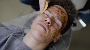 Güzellik uzmanlarının elleri, adamın yüzünü bir kahve fırçasının süngeriyle temizler.