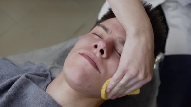 Widok kosmetyczki ręce wytrzeć twarz człowieka gąbką podczas zabiegu — Wideo stockowe