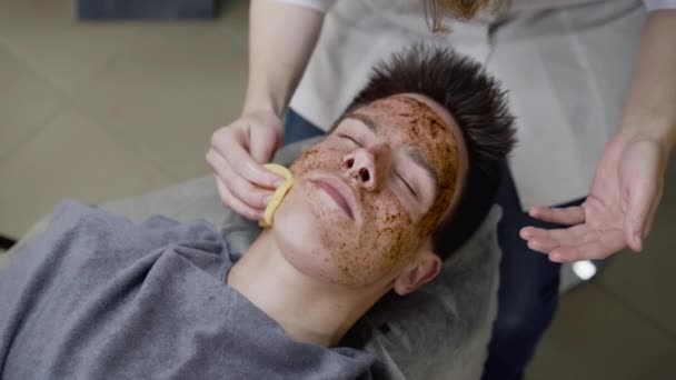 Widok kosmetyczki ręce wytrzeć peeling kawy z twarzy mężczyzn z gąbką — Wideo stockowe