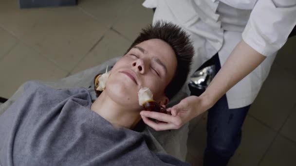 Чоловік отримує омолодження шкіри з масажем обличчя з равликами в салоні — стокове відео