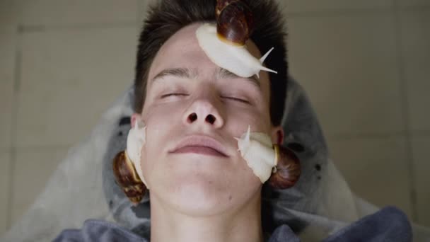 Horní pohled na mladého muže dostává masáž obličeje s šneky Achatina v lázních — Stock video