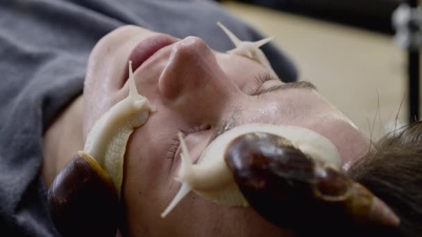 Процедура омоложения кожи с ползучими улитками Ачатина на мужском лице в спа — стоковое видео