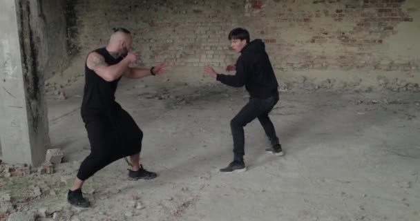 Skilful fighting of two angry men in black clothes in an abandoned building — Stock Video