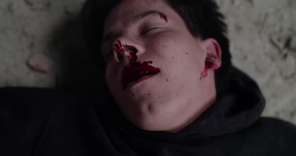 Portret van een gewonde, bebloede man ligt op een vloer en lacht door de pijn — Stockvideo