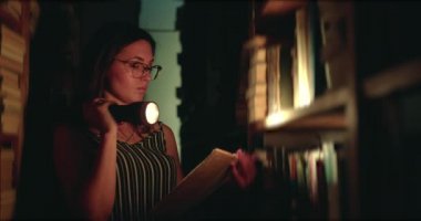 Karanlık kütüphanede kitap okuyan gözlüklü kız.