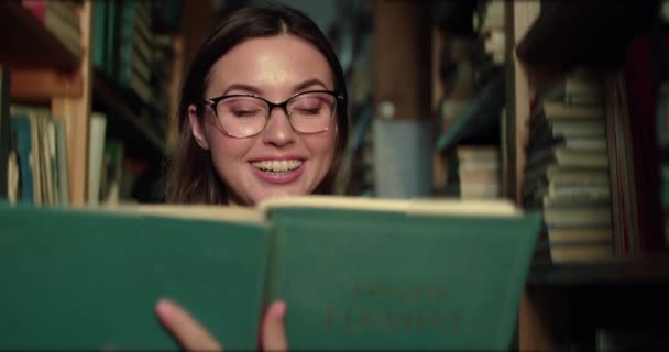 ผู้หญิงในแว่นตาดูเกี่ยวกับหนังสือความสุขและความมหัศจรรย์ใกล้ชั้นวางในห้องสมุด — วีดีโอสต็อก