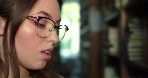 Detailní profil dívky v brýlích vedoucí oči během čtení v lirbary — Stock video
