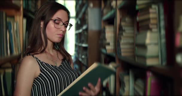 A lány elolvassa a könyvet a könyvtárban, becsukja, a kamerába néz és egy hüvelykujját mutatja. — Stock videók