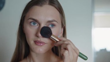 Makyaj fırçası, fırçayla makyaj tozu süren gülümseyen bir kadının yüzü. Stüdyodaki gri arka planda mutlu ve izole. Portre, kozmetik ürün ve modelin tozu, cilt temeli ve yüz güzelliği. Kapat.