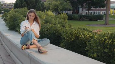 Çekici bir kadın deftere not alıyor dışarıda tek başına oturuyor. Gülümseyen akıllı kız parkta günlüğe düşünceler yazıyor. Kendine güveni tam bir yazar. Elinde kağıt not defteri var.