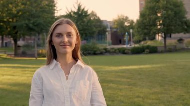 Beyaz gömlekli zarif bir öğrenci üniversitenin önündeki kameraya bakıyor. 4K
