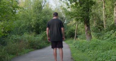 Yeşil bahar ormanlarında bir adam yolda yürüyor, tek ayağı üzerinde topallayarak, 4k