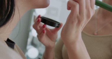 Makyaj sanatçısı olarak genç beyaz bir kızın yakın çekimi bir müşterinin yüzüne makyaj tozu sürer. 4K