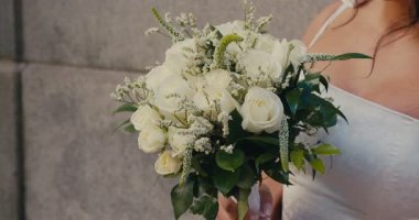 Beyaz elbiseli, elinde elmas bir yüzükle gelin tarafından tutulan bir buket beyaz gülün yakın çekimi. Güzel, iri yarı bir kadın. Ağır çekim. 4K.