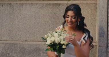 Beyaz elbiseli, elinde elmas bir yüzükle gelin tarafından tutulan bir buket beyaz gülün yakın çekimi. Güzel, iri yarı bir kadın. Ağır çekim. 4K.