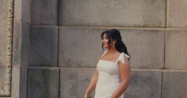 Beyaz gelinlik içinde elinde buket tutan güzel bir gelin klasik mimarisi olan eski bir taş binanın önünde duruyor. Ağır çekim. Büyük boy model.