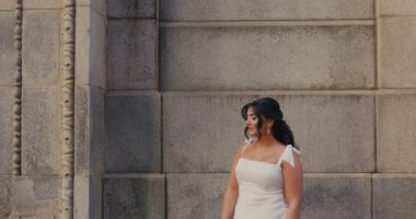 Beyaz gelinlik içinde elinde buket tutan güzel bir gelin klasik mimarisi olan eski bir taş binanın önünde duruyor. Ağır çekim. Büyük boy model.