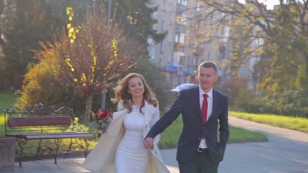 Mladá žena a muž kráčející v městském parku se drží za ruce — Stock video