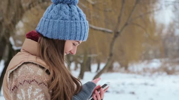Девушка разговаривает по смартфону в зимнем парке — стоковое видео