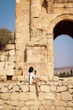 Antik taş duvarda akıllı telefon kullanan genç bir kadın. Jerash. Jordan.