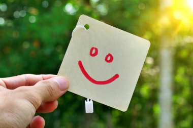 Mutluluk ve pozitiflik kavramı. Güneşte basit bir mutlu yüz sembolü tutan bir el.