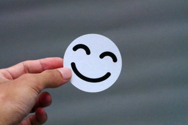 Basit gri bir arkaplana karşı beyaz gülen yüz ikonu tutan bir insan eli.