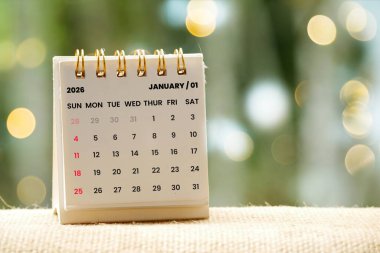Küçük bir masa takvimi, Ocak 2026 'yı bulanık bir bokeh arkaplan ile dokulu bir yüzey üzerinde gösteriyor.