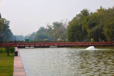 Delhi, Hindistan, 28 Kasım 2025. Kartavya Yolu Parkı 'ndaki su kanalının manzarası. Kırmızı kumtaşı köprüsü ve arka planda sarı çekçekçekler var..