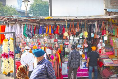 Nanded, MH, India, 21 Aralık 2025: Seyyahlar ve yerliler güneşli bir günde Gurudwara pazarının yakınlarındaki renkli el çantaları, çantaları ve aksesuarları sergileyen işlek bir yol kenarında alışveriş yapıyorlar.