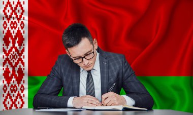 Ceketli ve gözlüklü bir işadamı masaya oturur ve Belarus 'un arka planına karşı bir sözleşme imzalar.