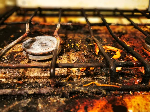 Dirty and rusty top of a kitchen gas stove with pieces of debris, food and burning, dirt stains, used for cooking.