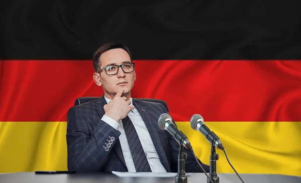 Young man in glasses and a jacket at an international meeting or press conference negotiations, on the background of the flag germany