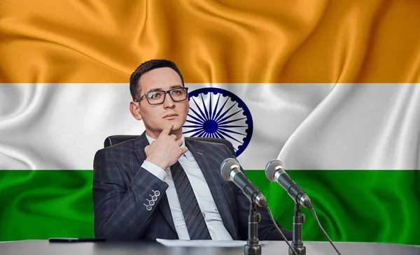 Young man in glasses and a jacket at an international meeting or press conference negotiations, on the background of the flag India
