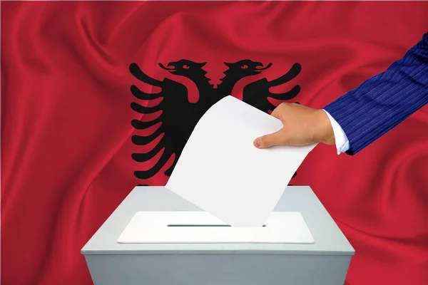 Elections in the country - voting at the ballot box. A man\'s hand puts his vote into the ballot box. Flag Albania on background.