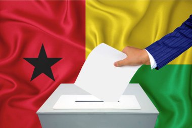 Ülkedeki seçimler - oy sandığında oy kullanma. Bir adam oyunu sandığa koyuyor. Arka planda Gine Bissau bayrağı.