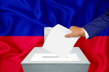 Ülkedeki seçimler - oy sandığında oy kullanma. Bir adam oyunu sandığa koyuyor. Arka planda bayrak haiti.