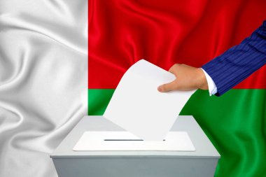 Ülkedeki seçimler - oy sandığında oy kullanma. Bir adam oyunu sandığa koyuyor. Arka planda Madagaskar bayrağı.