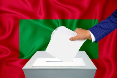 Ülkedeki seçimler - oy sandığında oy kullanma. Bir adam oyunu sandığa koyuyor. Arkaplanda Bayrak Maldivleri.